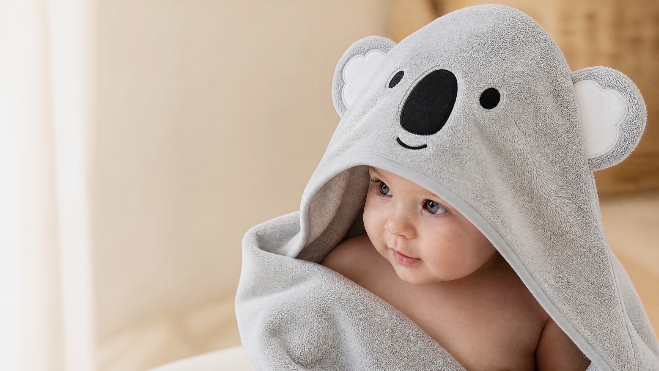 Baby wrapped in the grey MiniBoo Koala hooded towel, in a warm morning room